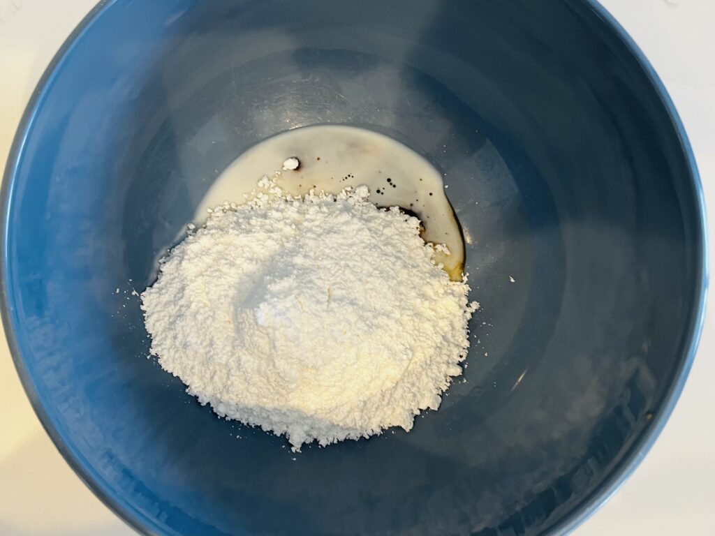 Powdered sugar, vanilla and milk in a mixing bowl.