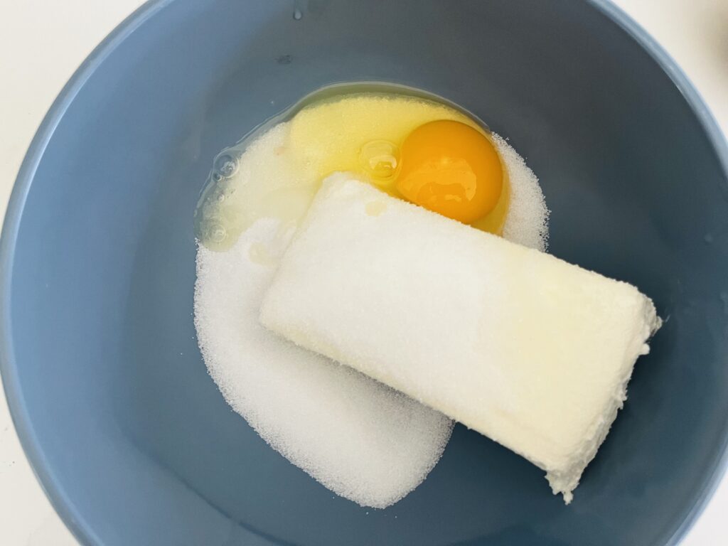 Cream cheese, an egg and sugar in a mixing bowl.