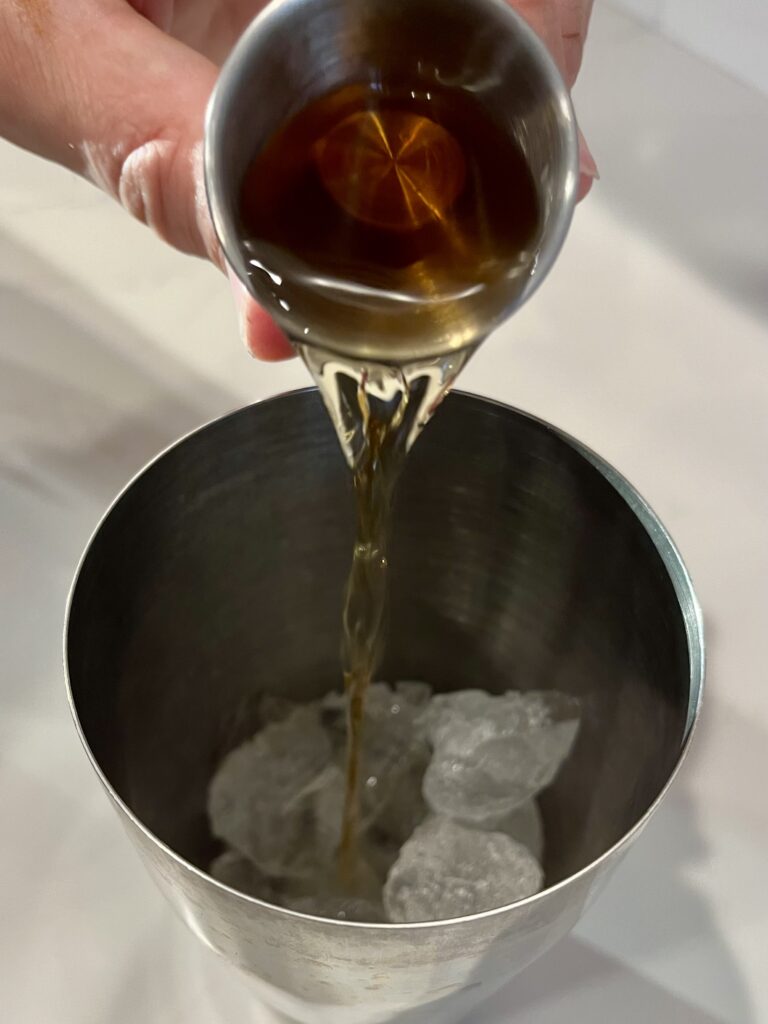 Pouring apple infused whiskey into a cocktail shaker.
