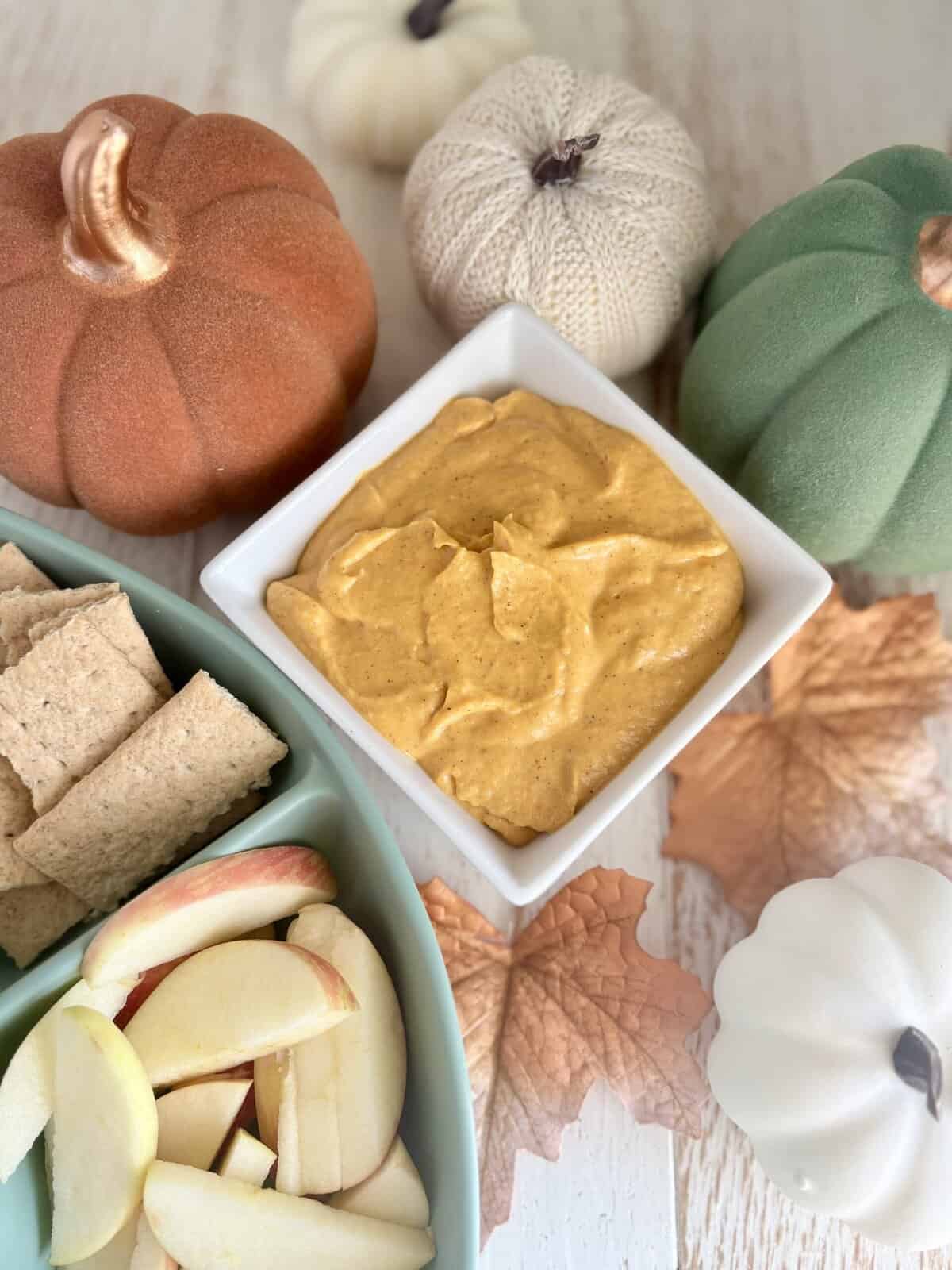 pumpkin dip in a bowl next to a tray of apples and graham crackers