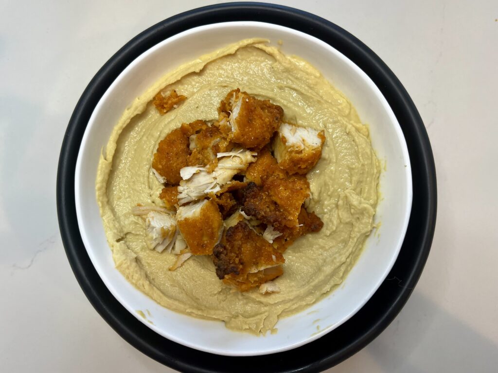 Chicken on top of hummus in a bowl.