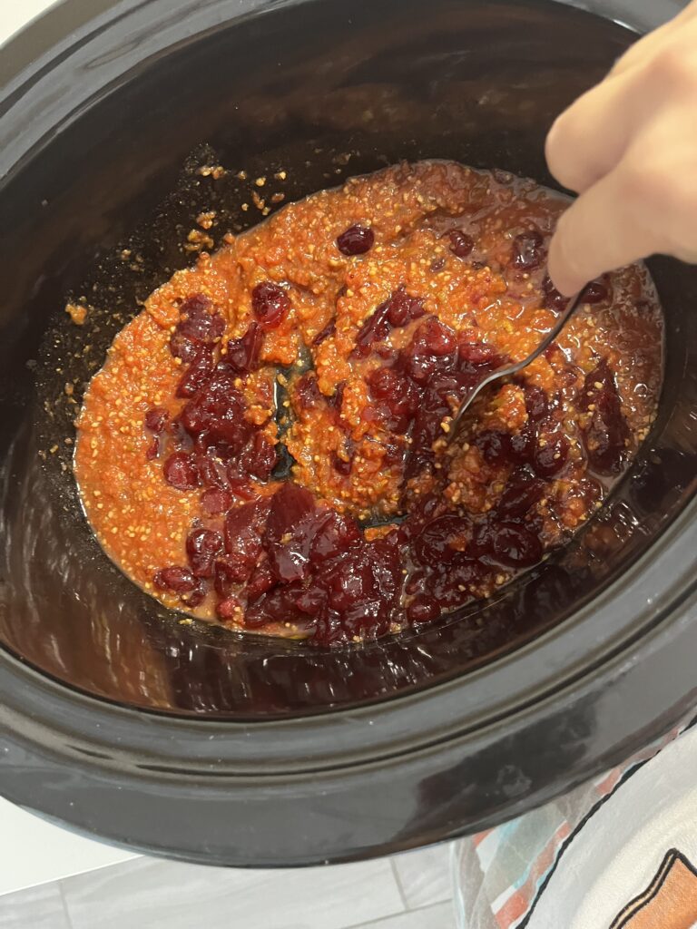 Using a spoon to mix salsa and cranberry sauce in a slow cooker.