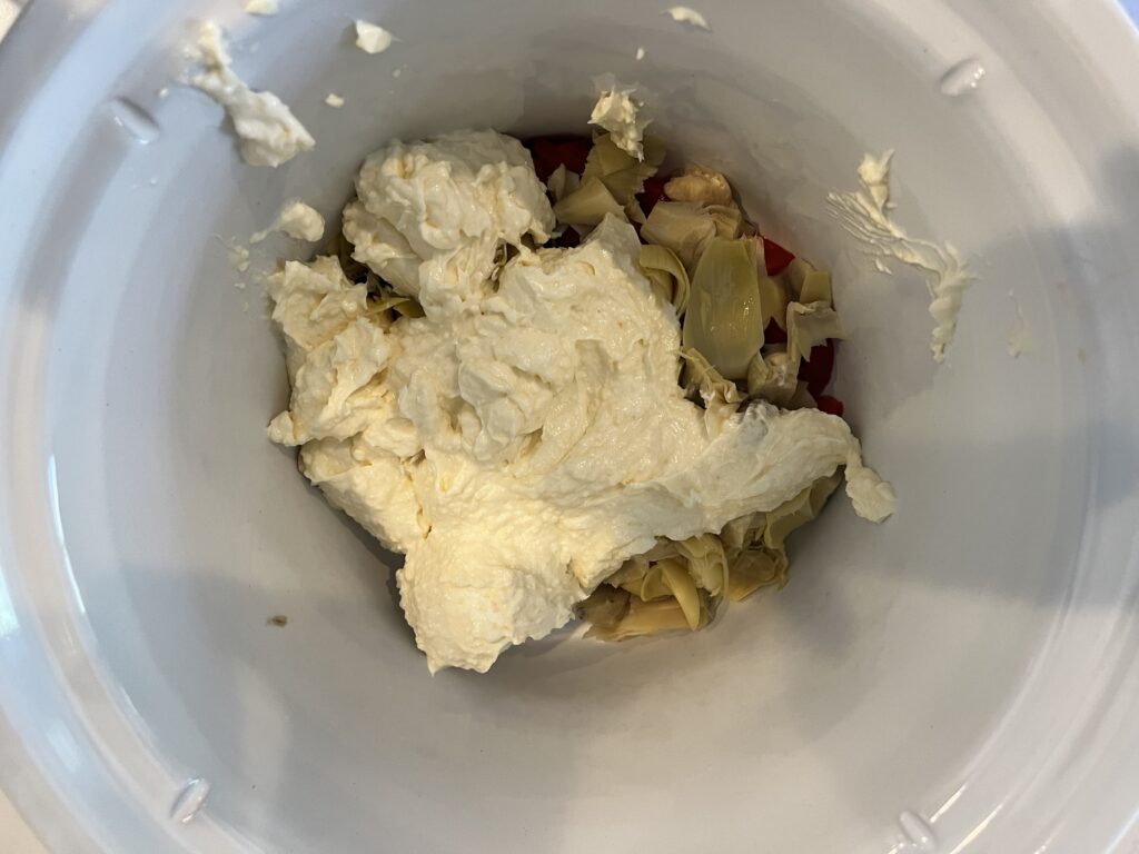 Cheese mixture and chopped artichokes and roasted red peppers in a slow cooker.