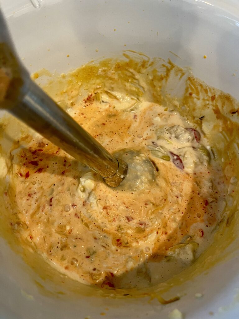 an immersion blender blending cooked dip in a slow cooker