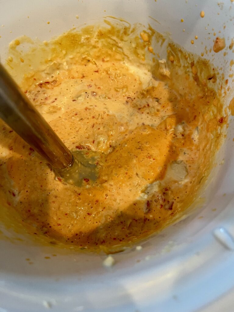 an immersion blender blending cooked dip in a slow cooker making it creamy.