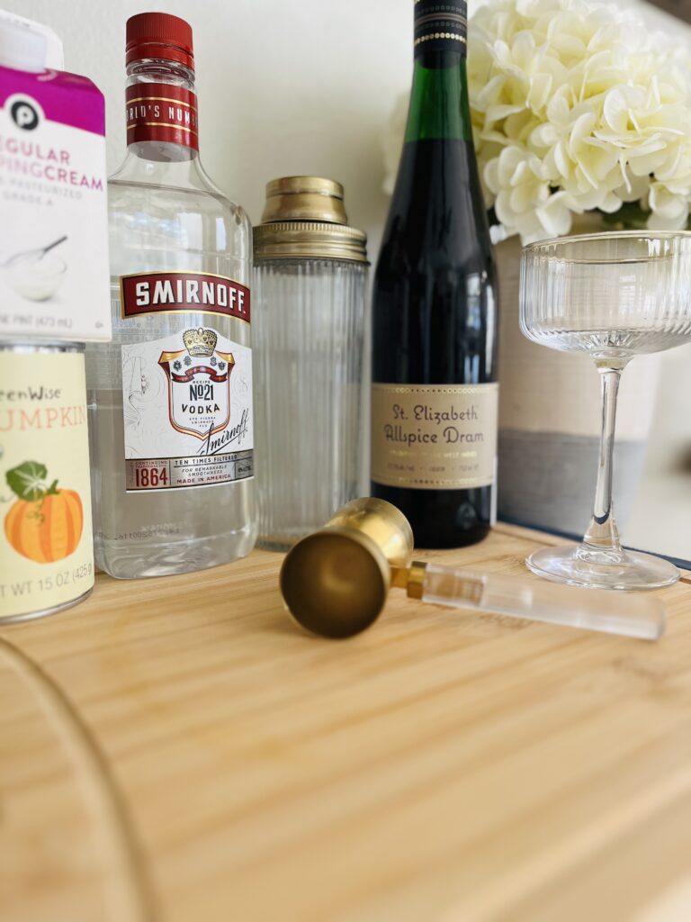 Heavy cream, pumpkin pure, allspice dram liqueur and vodka on a cutting board on a counter.