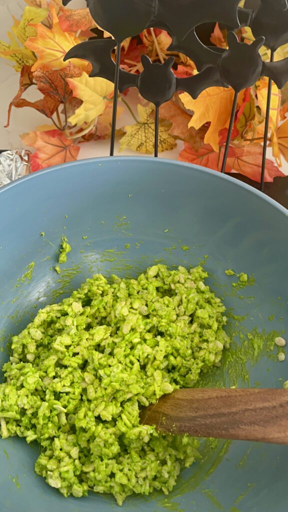 A spoon mixing neon green rice crispy cereal in a blue bowl on the counter.