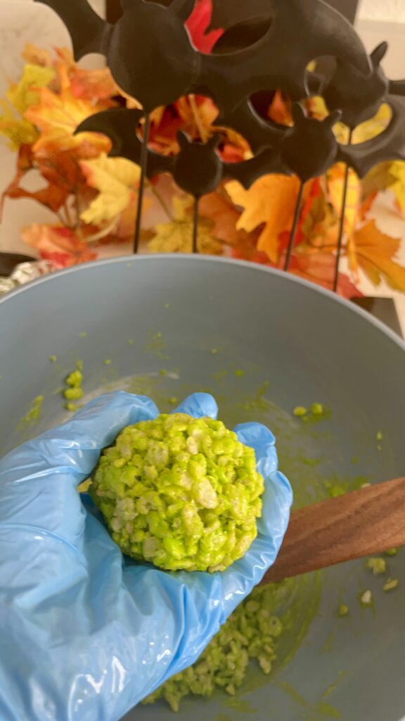 Holding a neon green rice crispy treat in gloved hand.