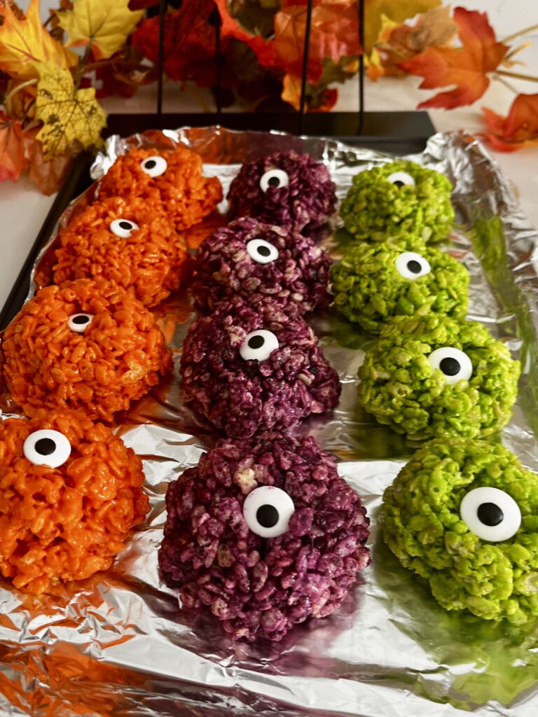 a lined baking sheet with neon green, purple and orange creepy crispy eyeball treats on the counter.