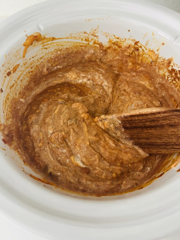 Stirring bean dip ingredients in a slow cooker on the counter.