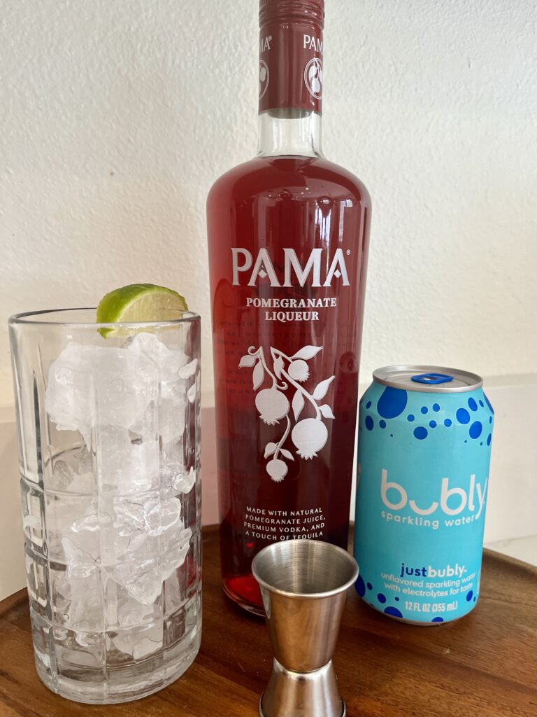 pomegranate liqueur , unflavored sparkling water and a tall glass filled with ice with a lime wedge on a tray on the counter