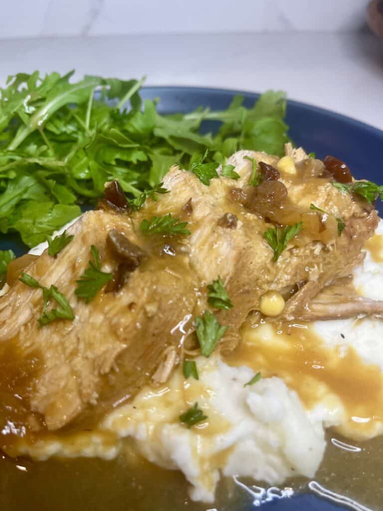 Savory pork tenderloin with creamy gravy and fresh herbs served with mashed potatoes and side greens on a blue plate.