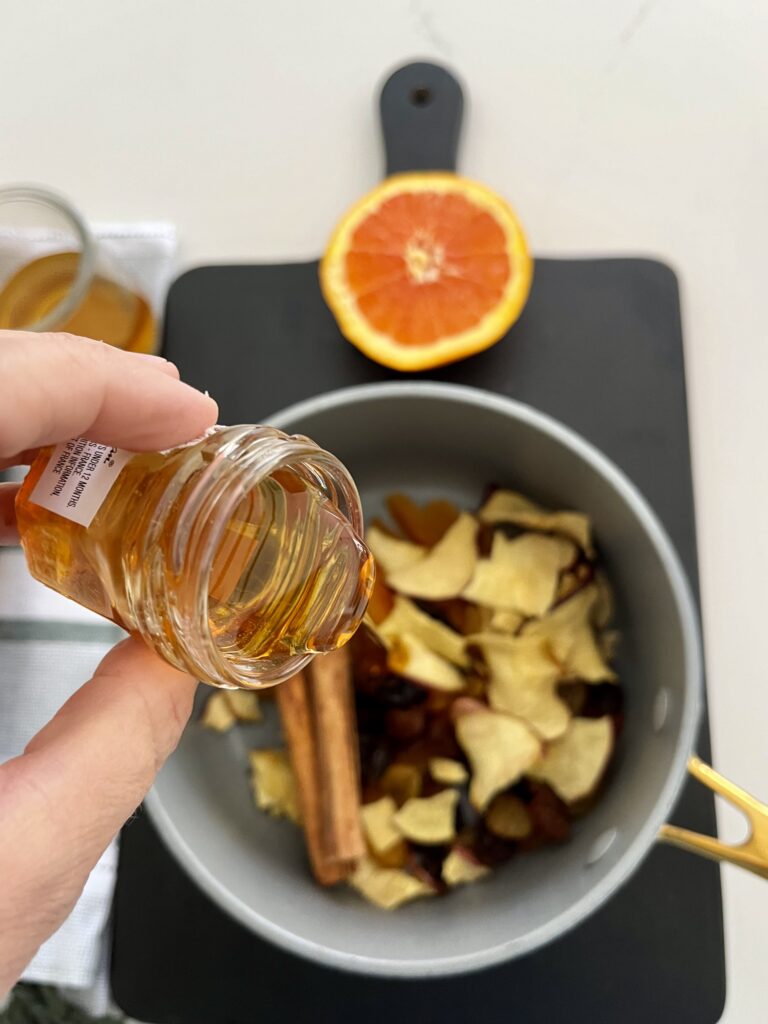 Honey being poured into a pot filled with dried fruit on a black cutting board on the counter.