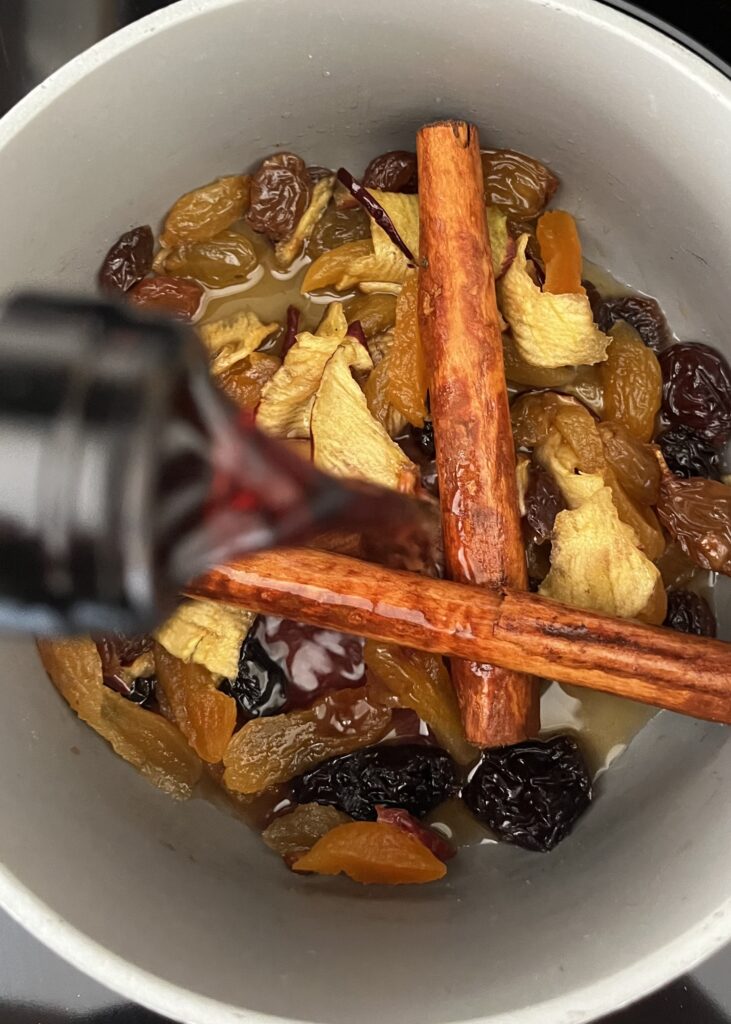 Red wine being poured over top of the fruit and brandy mixture in a pot on the stove.