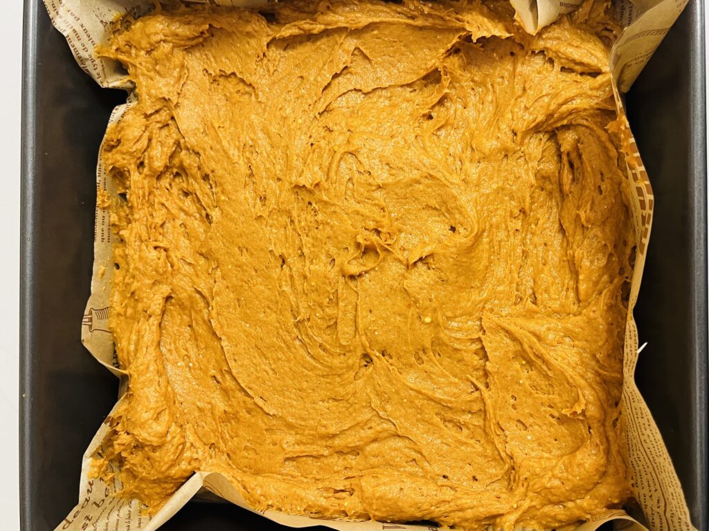 spice cake batter in a parchment paper lined 9x9 cake pan on the counter.