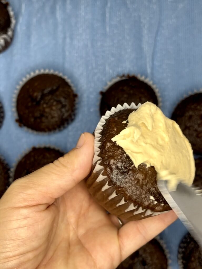 Icing a chocolate cupcake in hand.