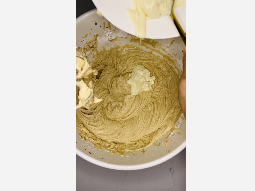 Pouring melted white chocolate into a large white bowl on the counter