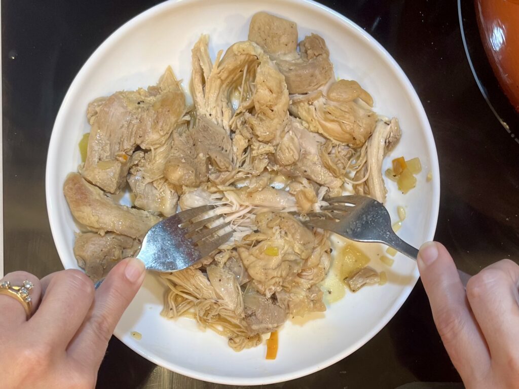 chicken being shredded with two forks on a plate 