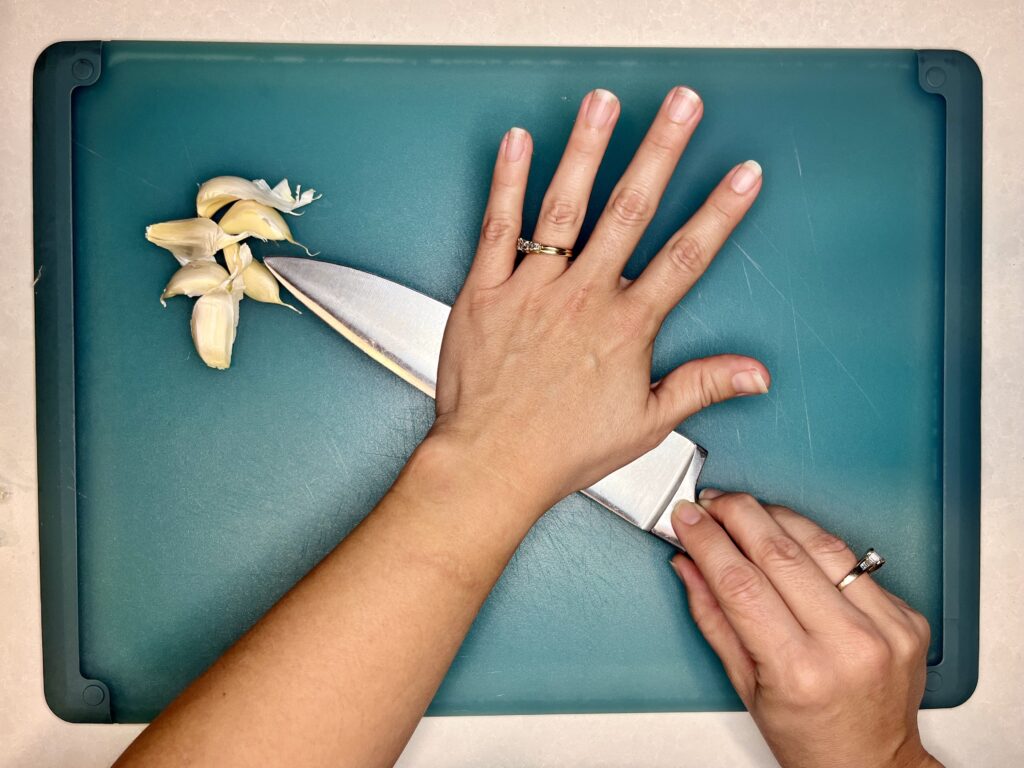 a garlic bulb being smashed with the flat side of a knife 