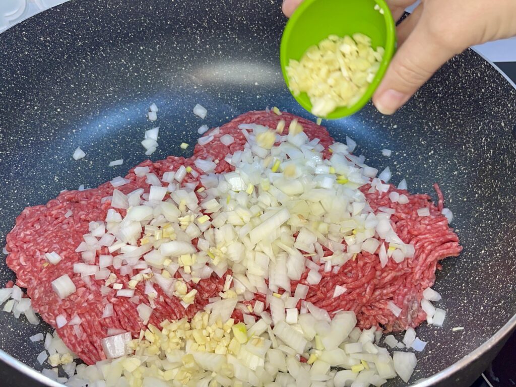 minced garlic being added to pan with beef and onion