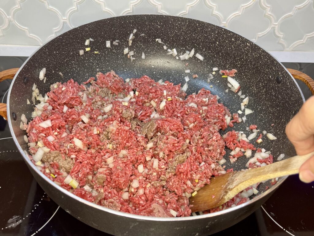 a wooden utensil string beef, garlic and onion in a pan