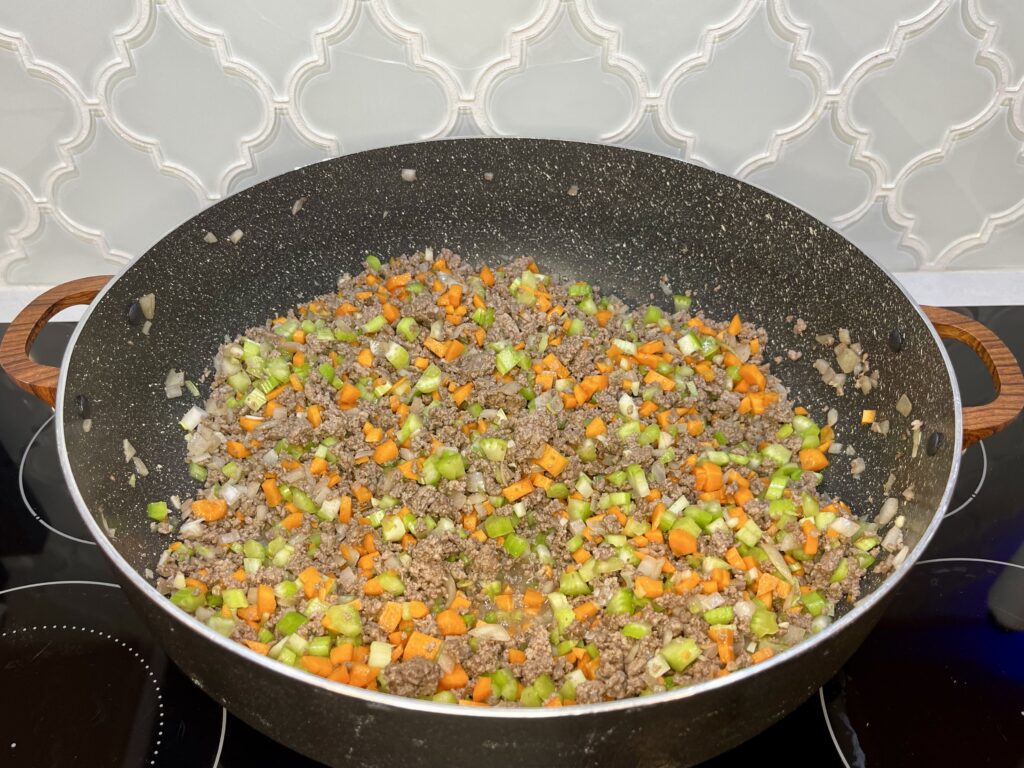 a pan with cooked beef, onion and garlic and freshly added celery and carrots