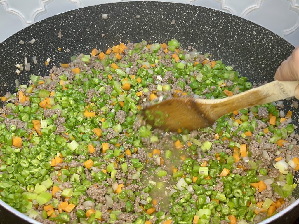 green beans being stirred into beef mixture