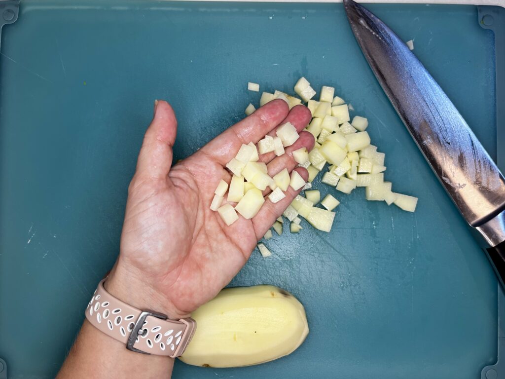 a hand showing potato finely diced on a cutting board with a knife.