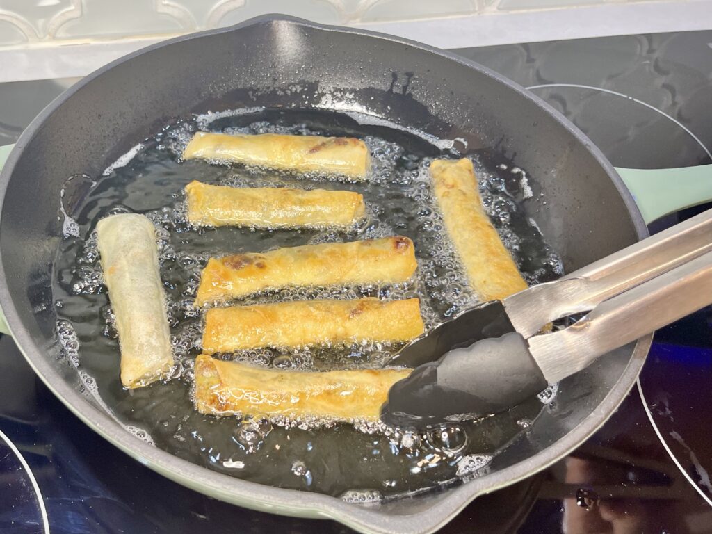 lumpia being turned by tongs in a pan with hot oil