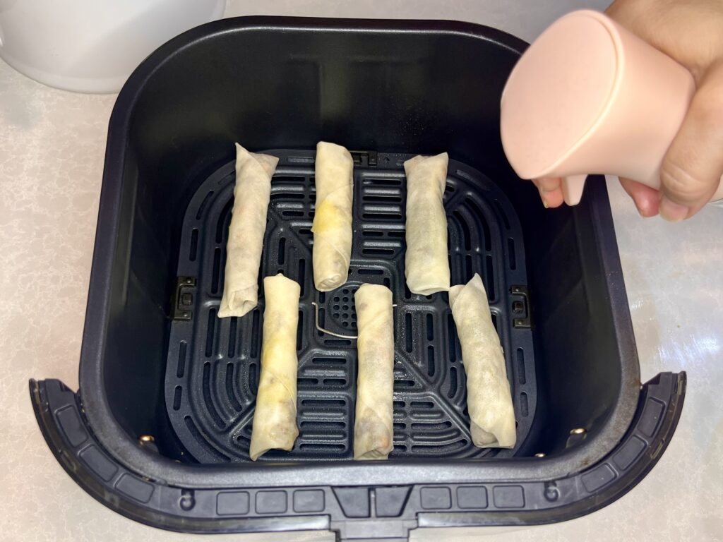 lumpia in an air fryer basket being spritzed with oil