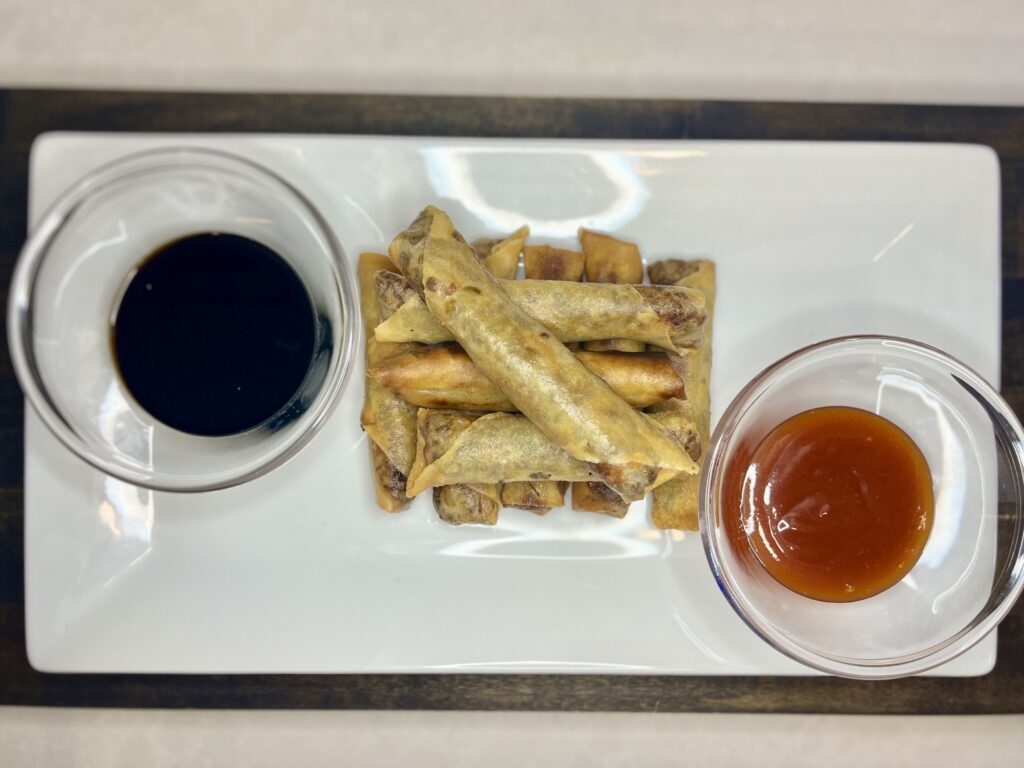 a plate with lumpia, a dipping bowl of soy sauce, and a dipping bowl of sweet and sour sauce