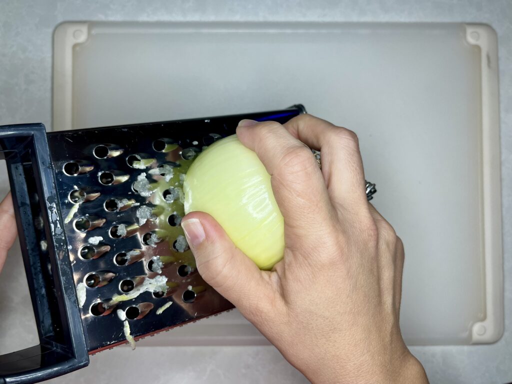 an onion being grated with a box grater