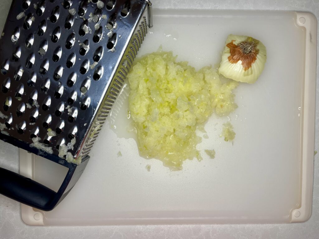 grated onion on a cutting board next to a grater