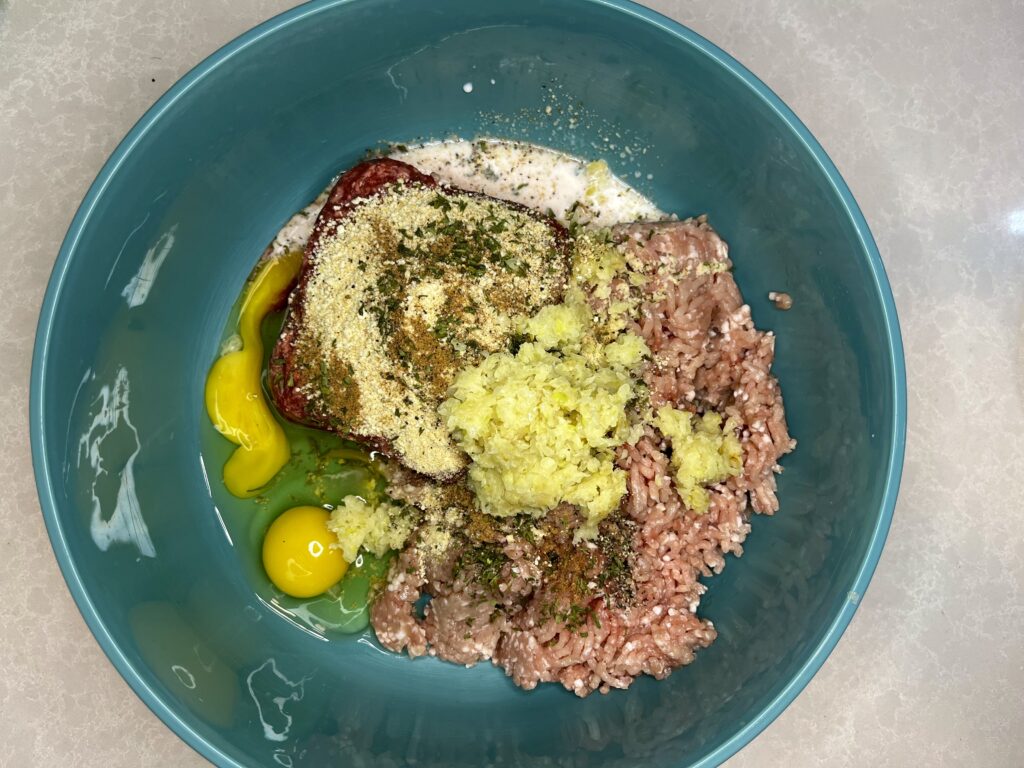 pork, beef, breadcrumbs, eggs, seasoning, milk and cooked onions in a bowl