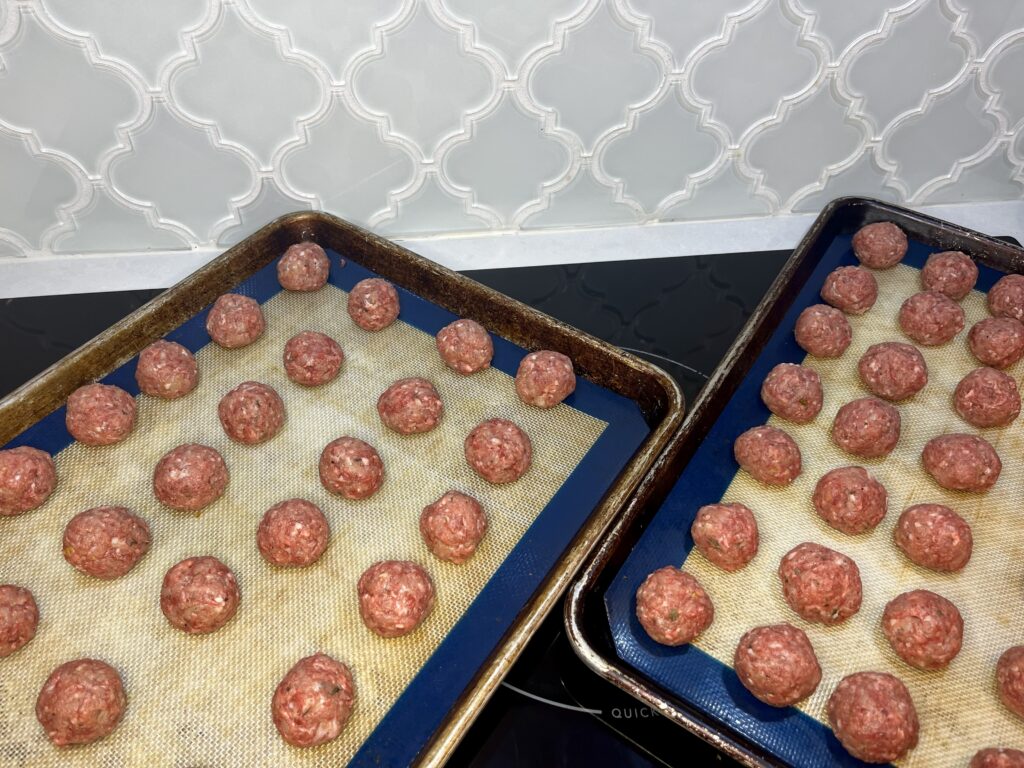 baking sheets with uncooked meatballs ready for the oven