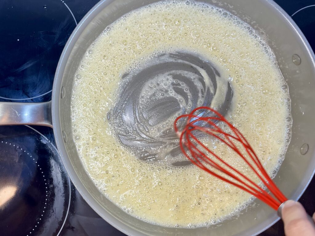 flour and butter being whisked while cooking on a stove