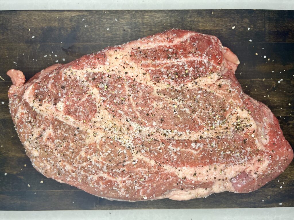 a raw chuck roast seasoned with salt and pepper