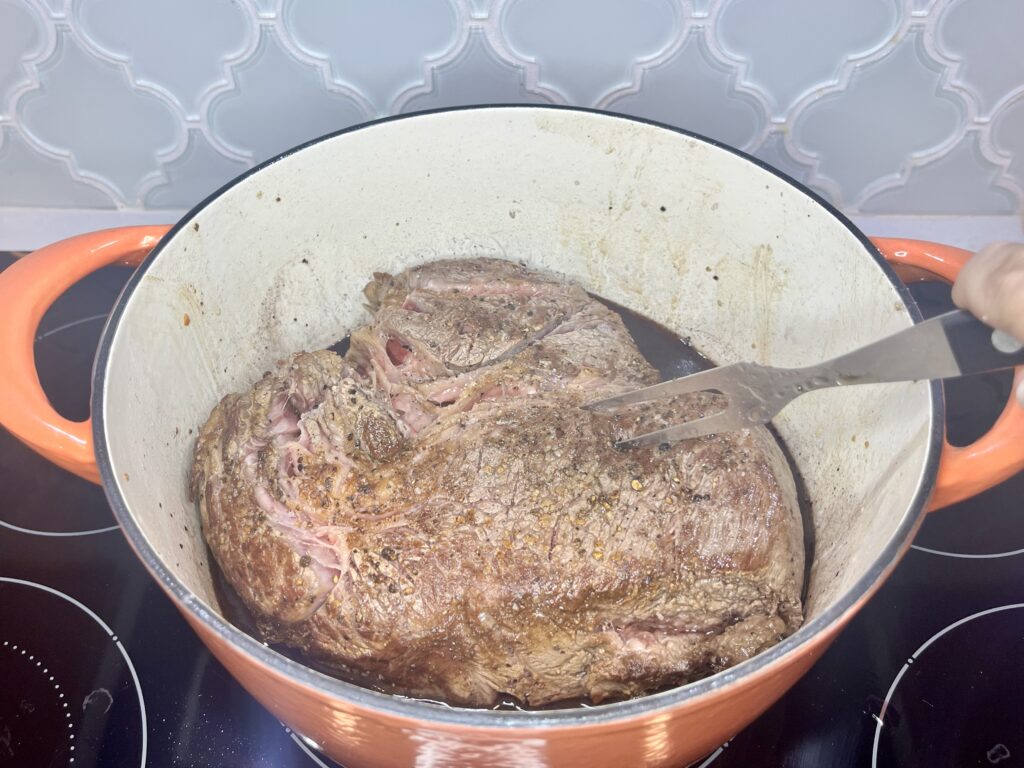 A chuck roast being added back to a pot on a stove