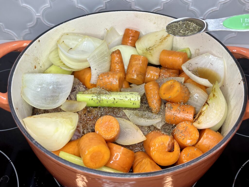 a pot filled with beef, vegetables, and broth with thyme being added