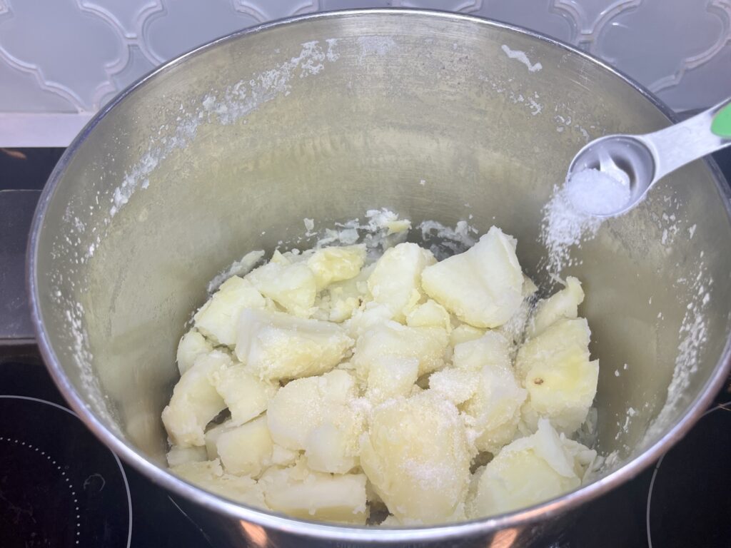 salt being added to a pot of cooked potatoes 