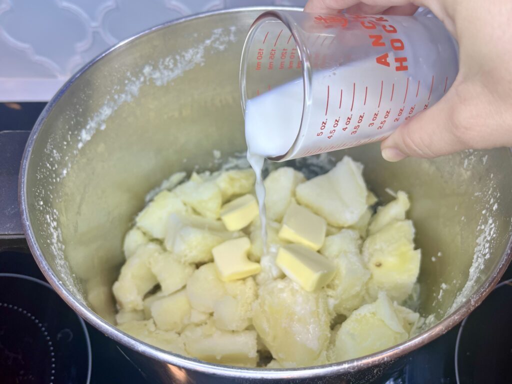 Milk being added to a pot with potatoes and butter 