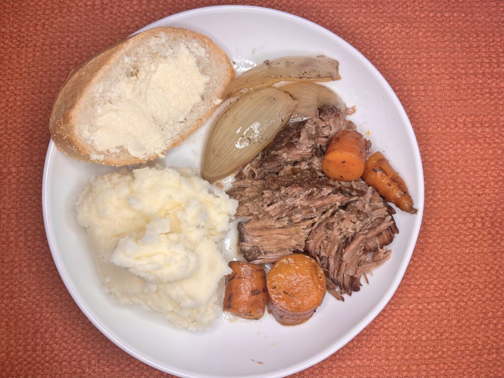 a plate with pot roast, mashed potatoes, and buttered bread 