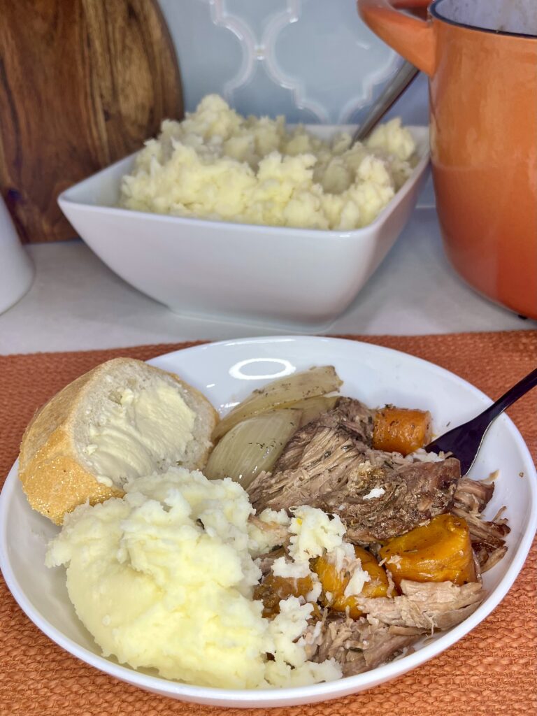 a plate with pot roast, mashed potatoes and buttered bread with a bowl of cooked mashed potatoes