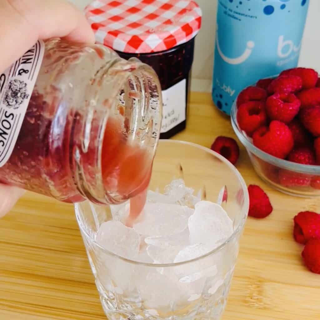 Pouring the shaken, vodka and citrus juice and the jam that has been shaken in a jam jar over a cocktail glass filled with ice