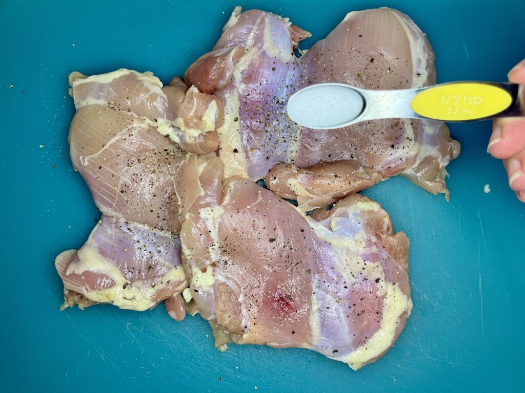 salt being sprinkled onto chicken thighs