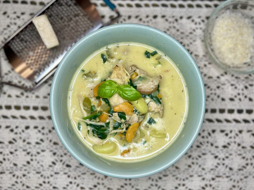 a bowl of chicken and gnocchi soup with parmesan cheese and basil