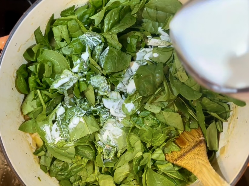 half and half being poured over spinach in a pot with vegetables and chicken 