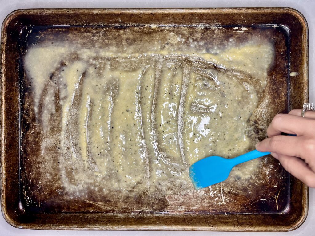 butter, seasoning and parmesan being spread over a baking sheet