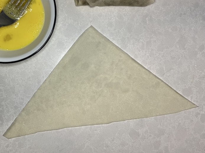 a triangle shaped lumpia wrapper with egg wash on a counter