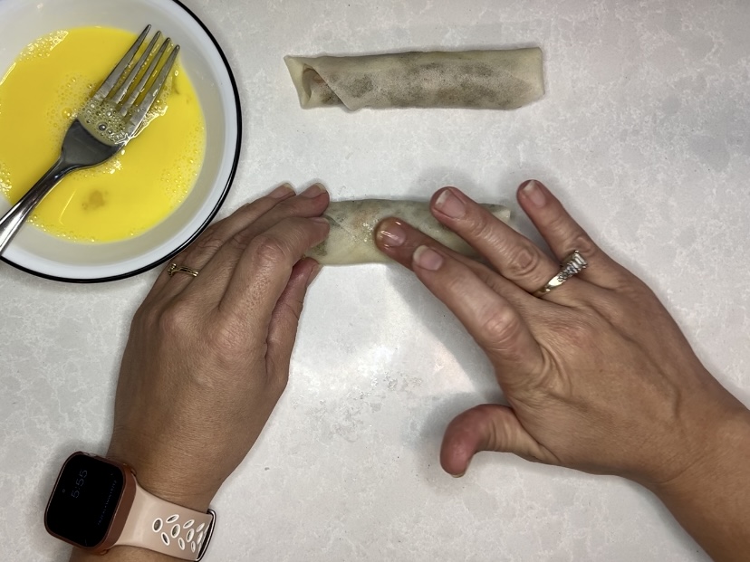 egg wash being applied to lumpia to glue down flap